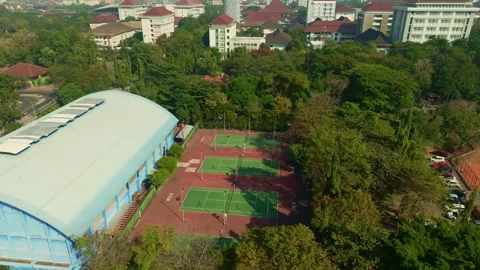Aerial tennis complex framed by trees and urban campus buildings Stock Footage 342588385