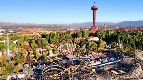 Aerial of theme park with rollercoaster rides and mountains in the background Stock Footage 291489835