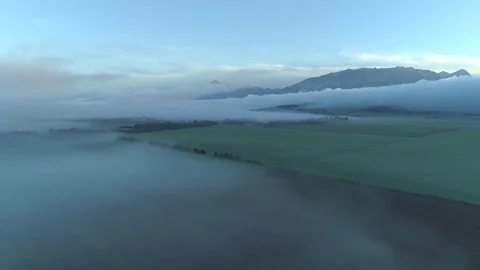 AERIAL Thick clouds of fog spreading across vast meadow fields in rural valley Stock Footage 80847546