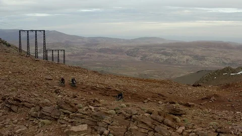 An aerial of three cyclists descending down a rocky slope into a desert valley. Stock Footage 127013364