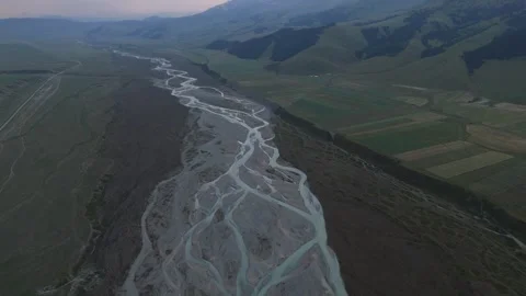 Aerial tilt up from a braided river to a mountain valley at dusk, Kyrgyzstan Stockbeeldmateriaal 347241053