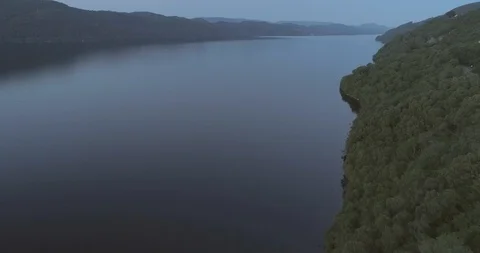 Aerial tilt down to where the forest meets the water of Loch Ness in the 스톡 동영상 112002314