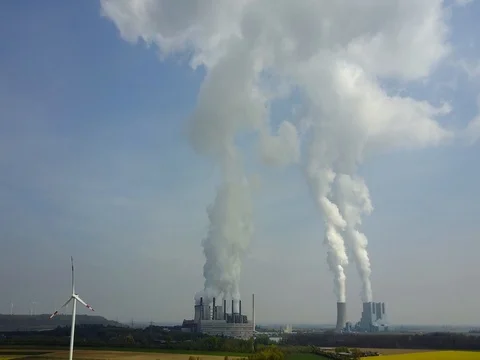 Aerial Tilt: Polution from smoking electrical power reactor next to windmill Stock Footage 79662636