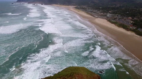 Aerial Tilt Up Shot Of Famous Haystack Rock In Wavy Sea At Beach Under Cloudy Video stock 260477669