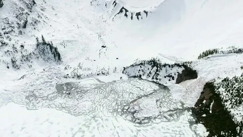 Aerial: Tilting down over avalanche debris flowing into frozen lake Stock Footage 72395293