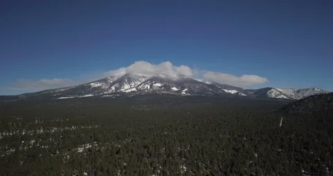 Aerial timelapse of clouds flowing switfly over snowy peaks above pine forest Stock Footage 101616994