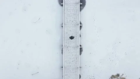 Aerial top down drone shot of person walking along snowy boardwalk Stock Footage 146294664