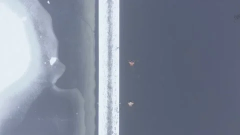Aerial top down drone shot of two people swimming in frozen lake Stock Footage 146294992