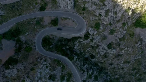 Aerial top down drone view of black car and bicycles traveling down a winding Stock Footage 254535947