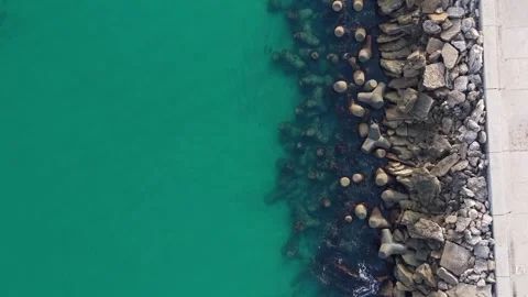 Aerial top-down drone view of rocky breakwater and turquoise water Stock Footage 322537444