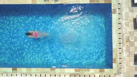 AERIAL TOP DOWN: Girl in pink bikini diving into empty pool at luxury resort Stock Footage