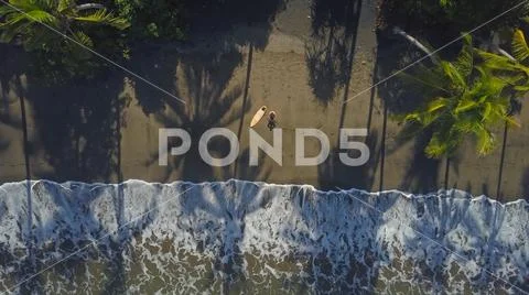 AERIAL, TOP DOWN: Lonely surfer sitting on sandy beach, looking into the horizon Stock Photos