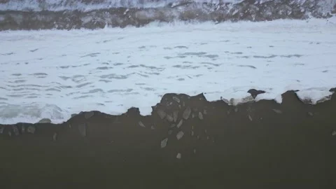 Aerial top down shot of broken off ice pieces washing against frozen sea shor Stock Footage 231050665