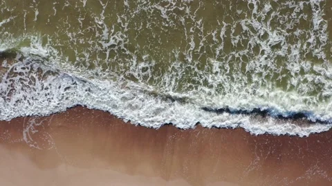Aerial top down shot flying along shoreline. Waves crashing against sand Stock Footage 157691547
