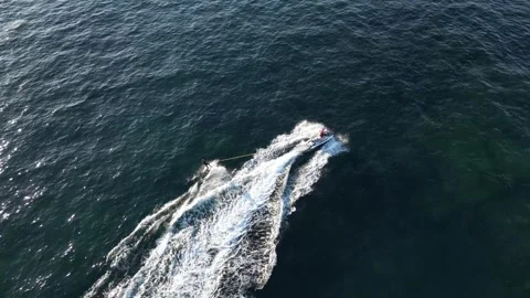 Aerial top down shot of jet ski pulling surfer on surfboard during sunny Stock Footage 248227360