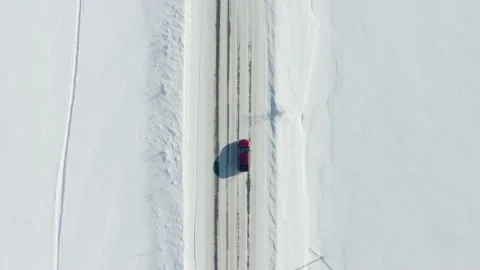 Aerial top-down shot of a red car or SUV driving along rural snowy road in Stock Footage 149057968