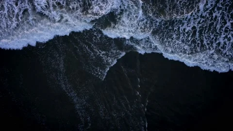 Aerial: Top down shot of Waves breaking on black sand beach Stock Footage 223973548