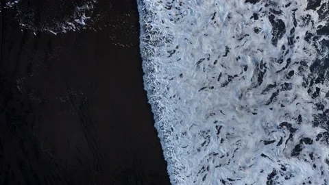 Aerial: Top down shot of Waves breaking on black sand beach Video stock 223973823