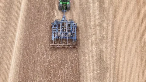 Aerial top down tracking follows tractor pulling mechanism on farmland in Stock Footage 286109457