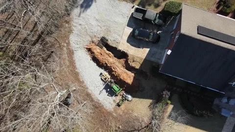 Aerial top down of tractor digging up septic tank in driveway Video stock 317025626