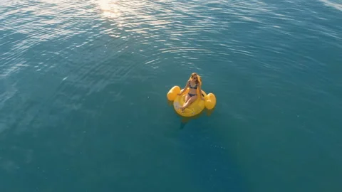 Aerial top down view of a beautiful woman relaxing on an inflatable yellow duck Stock Footage 112646416