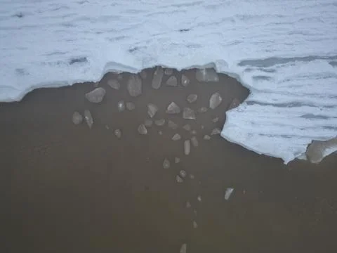 Aerial top down view of broken off ice pieces washing against frozen sea Stock Photos