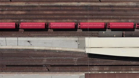 An aerial top-down view captures a vibrant red freight train traveling past a Stock Footage 337471750