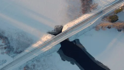 Aerial top down view of car driving across snowy road through winter bridge Stock Footage 123604942