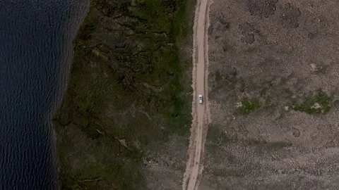 Aerial top-down view of a car driving by a shoreline of Sheosar Lake in Deosai Stock Footage 141757310