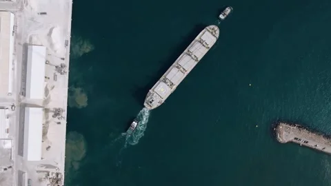 Aerial top down view of cargo ship guided by tugboats in port Video stock 344529030
