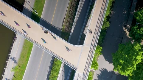 Aerial top down view of cyclists crossing footbridge in urban oasis Stock Footage 276424361