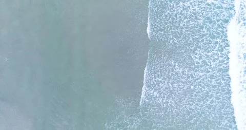 Aerial top down view of gentle ocean waves crashing on a sandy beach during.. Видео 327752689