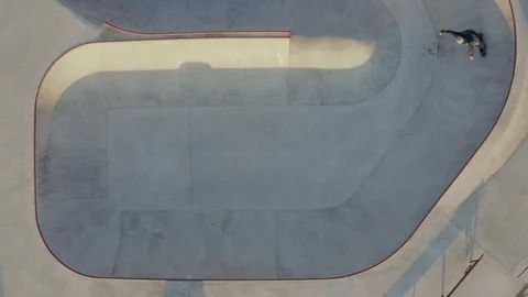 Aerial top-down view of guys riding skates across a large skatepark Stock Footage 128404177