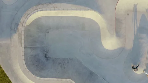 Aerial top-down view of guys riding skates across a large skatepark Stock Footage 128404215