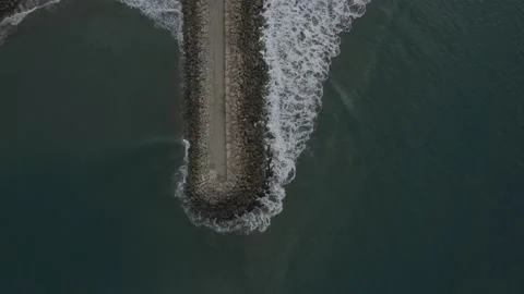 Aerial top down view of a large stone pier sticking out in the Pacific Ocean Stock Footage 146755321
