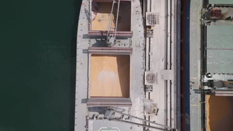 Aerial top-down view of a large cargo ship being loaded with grain at a port Stock Footage 345525115