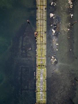 Aerial top-down view of a long wooden pier stretching across shallow coastal  Stock Photos