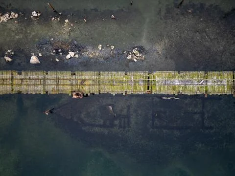Aerial top-down view of a long wooden pier stretching across shallow coastal  Stock Photos