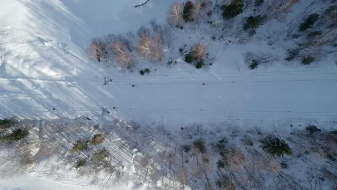 Aerial top down view of the moving ski-lift between the trees in winter. Skiers Video stock 163137364