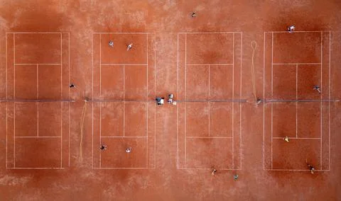 Aerial top-down view of multiple red clay tennis courts with players practicing Stock Photos