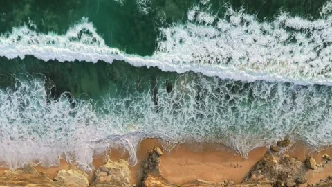 Aerial top down view of ocean surf and sandy coast with rocks. Powerful ocean Stock Footage 261652862