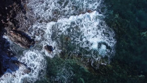 Aerial top-down view of ocean waves crashing against a rocky coastline Video stock 302002226