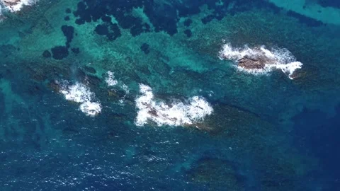 Aerial top-down view of ocean waves crashing against rocky reefs in a blue water Video stock 302002303