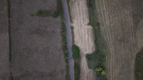 An aerial top-down view shows a single blue car driving along a straight rural Stock Footage 346888792