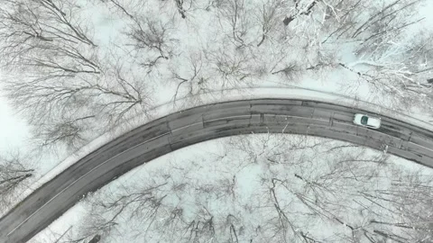 Aerial top-down view of snow covered pine forest and a road winding among trees 스톡 동영상 285396121