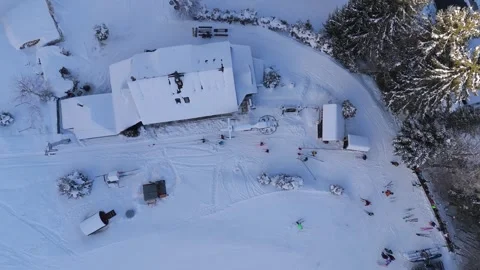 Aerial top down view of a snow covered mountain chalet and skiers at a winter Stock Footage 336384218