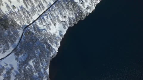 Aerial Top Down View of Snowy Lakeside Road with Vehicle Driving by Vast Lagoon Stock Footage 346618950