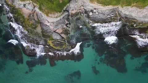 Aerial top-down view of turquoise sea waves crashing over rocky coastline with Stock Footage 310373289
