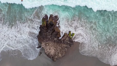 Aerial Top-Down View of Turquoise Ocean Waves Crashing against a Large Rock Stock Footage 334177472