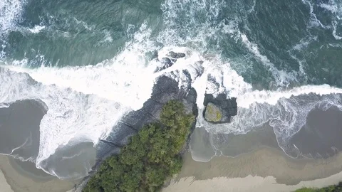 AERIAL Top-down view of waves crashing on beach with volcanic rock formation Stock Footage 119700385